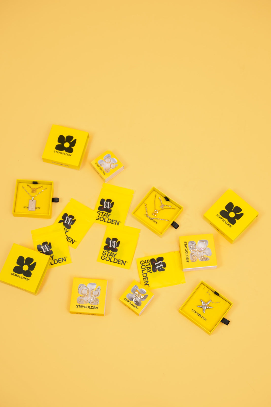 Stay Golden packaging flat lay: yellow slide boxes, window boxes, pouches and jewelry cards